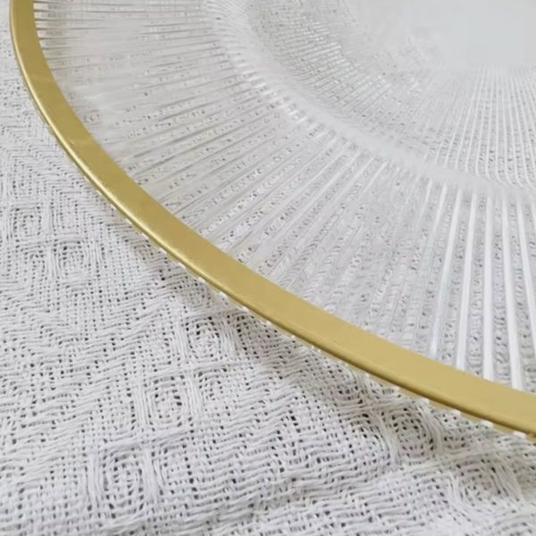Close up of a clear ribbed charger plate with gold rim on a net tablecloth